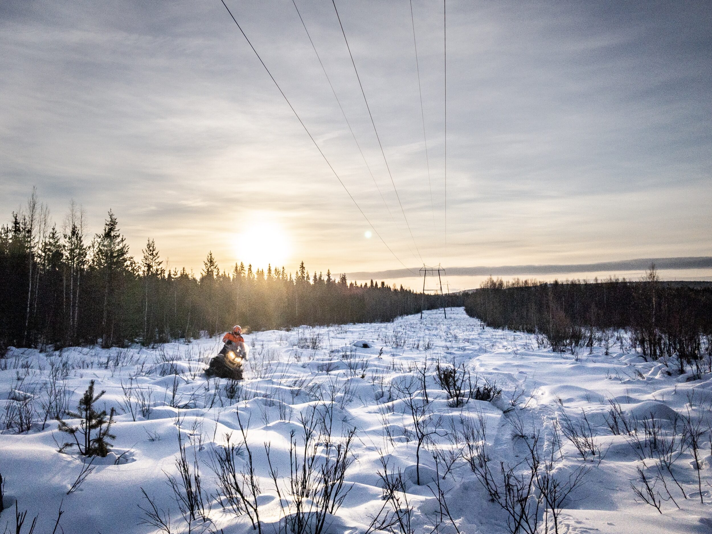 Verkostoasentaja moottorikelkalla sähkölinjan alla.